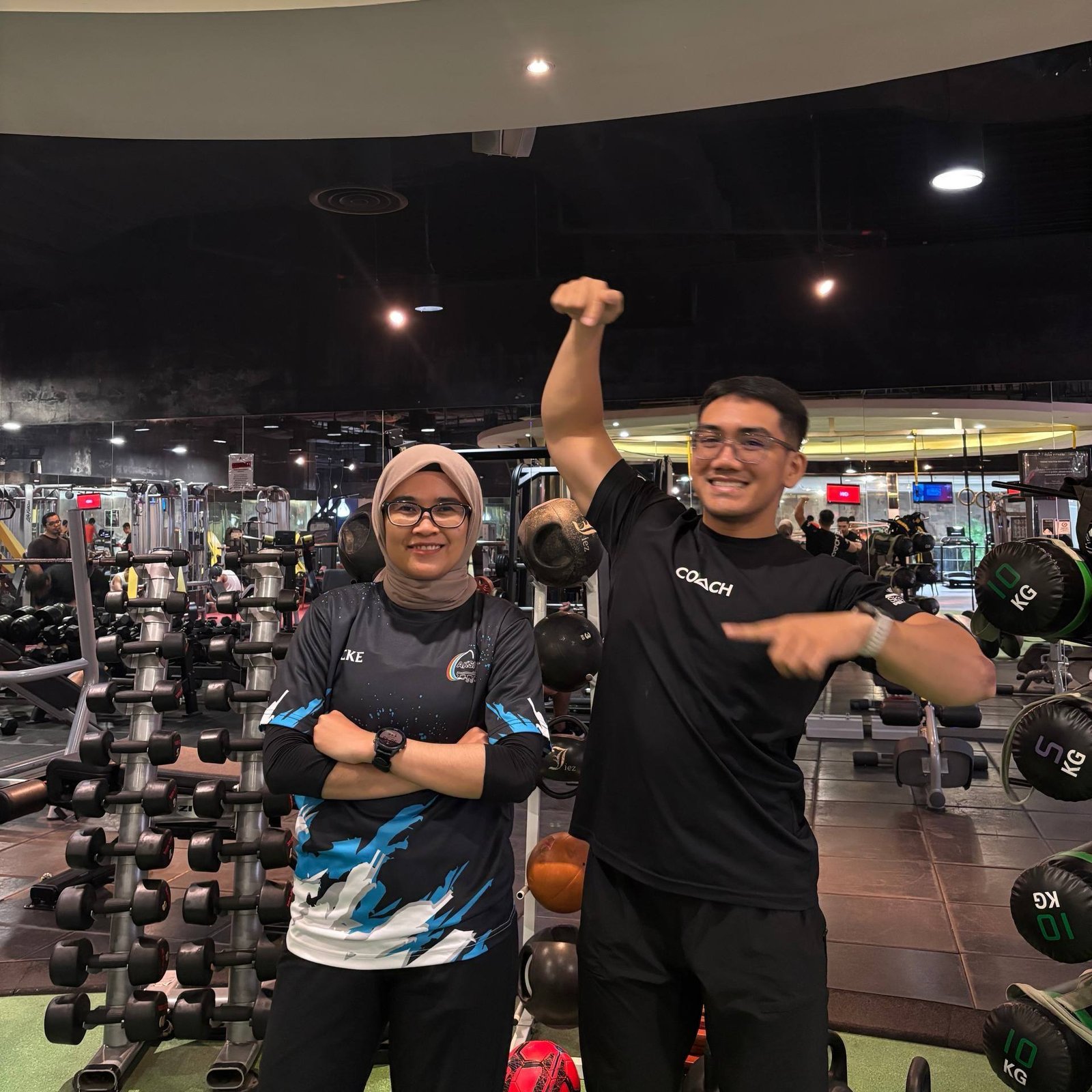 Faris and a client posing by the dumbbell rack